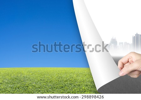 Woman hand turning gray cityscape page revealing nature sky grass, environmental protection concept