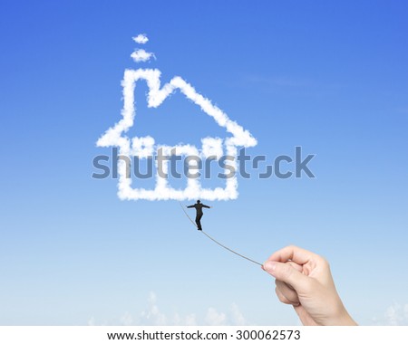 Businessman balancing on tightrope woman hand pulling, walking toward house shape clouds in blue sky.
