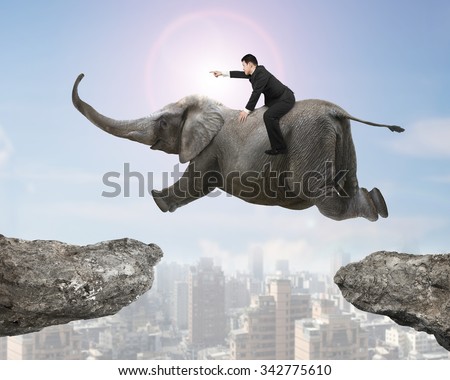 Man with pointing finger gesture riding elephant flying over two cliffs, with sunny sky cityscape background.