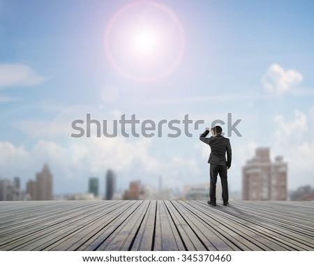 Rear view of black suit man standing gazing on wooden floor with sunny sky clouds cityscape background.