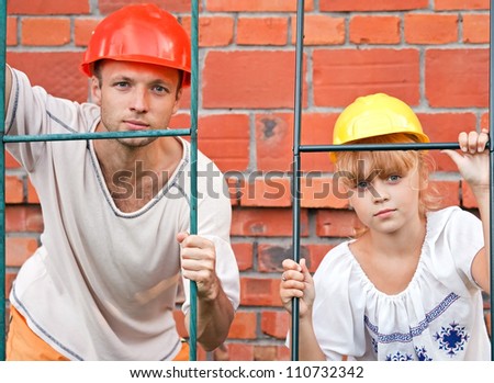 Portrait of young man and his little daughter as a construction workers with helmets