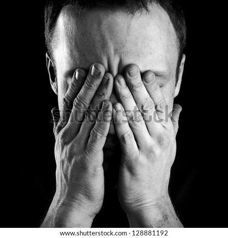 Monochrome Portrait Of Young Stressed Caucasian Man Covers His Face With Hands Isolated On Black Background
