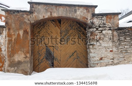 Stone wall of an ancient building with weathered wooden gate and snowdrift.Tallinn, Estonia