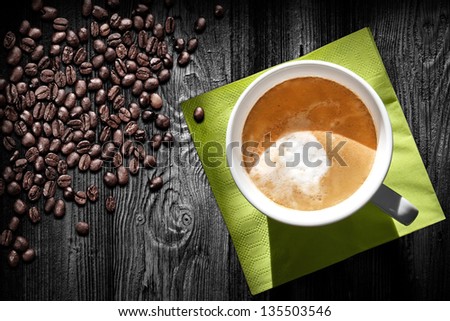 Cup of cappuccino coffee, green napkin and beans on black wooden table, top view