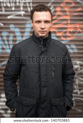 Portrait of young Caucasian man in black jacket with graffiti on a background