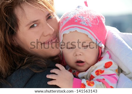 Young European woman holds her sleepy baby girl in blanket. Outdoor closeup portrait