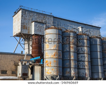 Row of gray tall tanks on old concrete factory