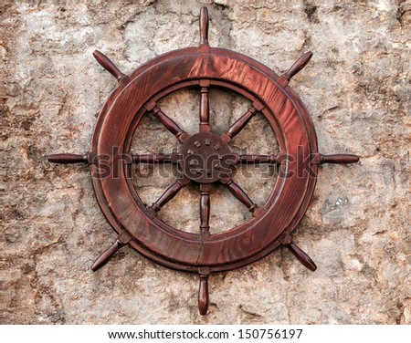Old wooden ship steering wheel on stone wall