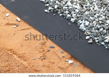 Geotextile layer between gray gravel and sandy ground
