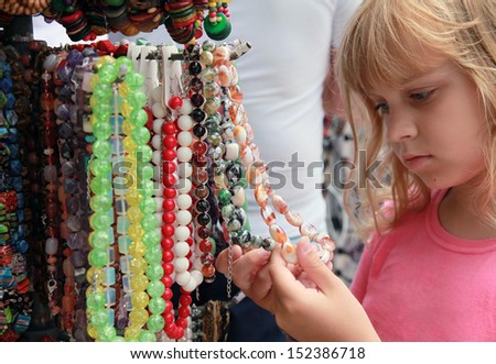 Little blond girl in the souvenir market considers colorful stone beads