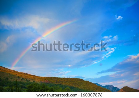 Mountain nature photo background with bright rainbow in dramatic cloudy sky