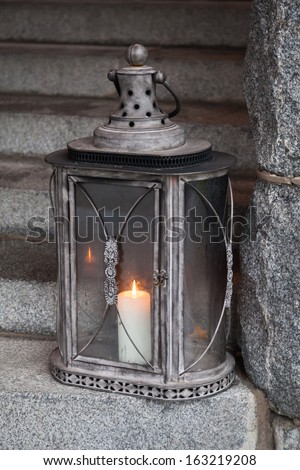 Old metal outdoor lamp with burning candle stands on stone stairs