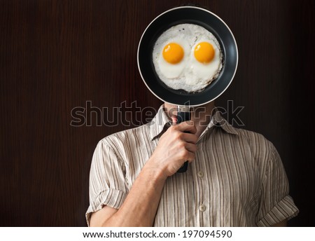 Young man portrait behind black frying pan with scrabbled eggs