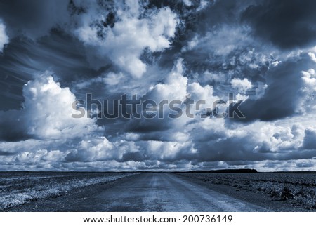 Empty asphalt country road under dark dramatic cloudy sky