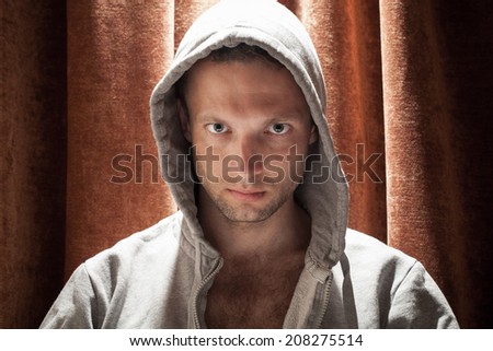 Portrait of young Caucasian man in the hood with red curtain background