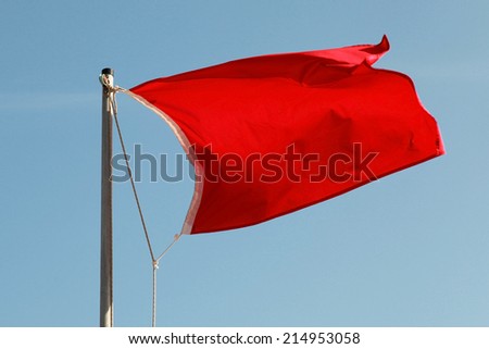 Red flag on a beach waving above blue sky