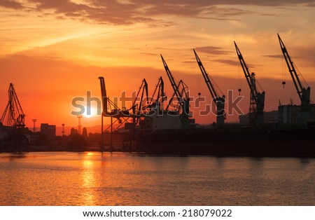 Silhouettes of cranes and industrial cargo ships in Varna port at sunset