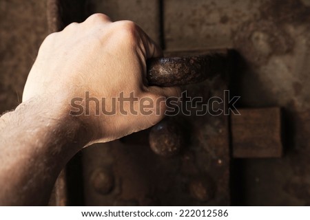 Male hand pull the handle of old rusted prison metal door with big lock