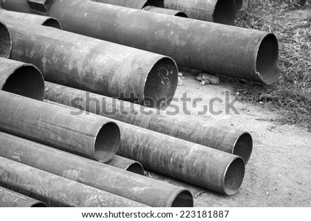 Rusted industrial steel pipes lay on the ground, monochrome photo