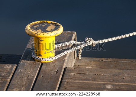 Yellow mooring bollard with nautical rope on wooden pier