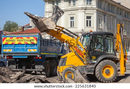 Ruse, Bulgaria - September 29, 2014: Road works. Highway maintenance, yellow tractor removes old asphalt pavement and loads it in a blue industrial truck