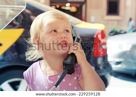 Outdoor portrait of little serious Caucasian blond girl talking on the street phone