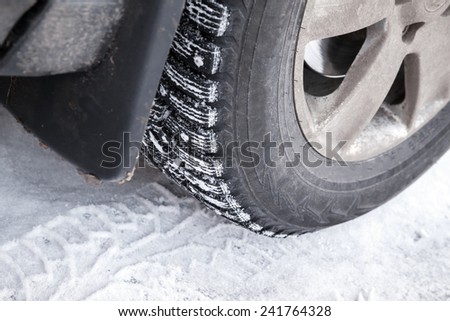 Fragment of modern automotive wheel with studded tires and winter snowy road