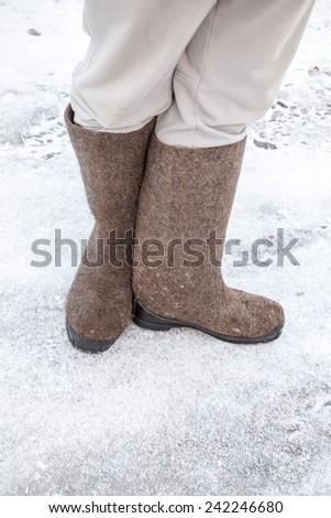 Feet with traditional Russian felt boots stand on winter road with snow and ice
