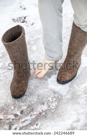 Male feet with traditional Russian gray felt boots stand on icy road