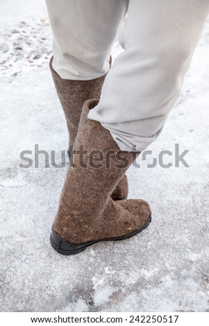 Male feet with traditional Russian felt boots stand on winter road with snow and ice