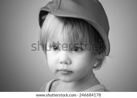 Black and white studio portrait of serious Caucasian baby girl in big baseball cap