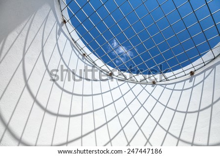 Abstract white interior fragment. Blue sky behind the round window with metal grid