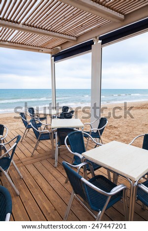 Open space bar interior with wooden floor and metal armchairs on the sandy beach