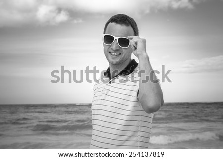 Outdoor monochrome portrait of young smiling Caucasian man in white sunglasses on summer ocean coast