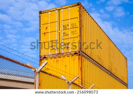 Yellow metal industrial cargo containers are stacked under blue cloudy sky