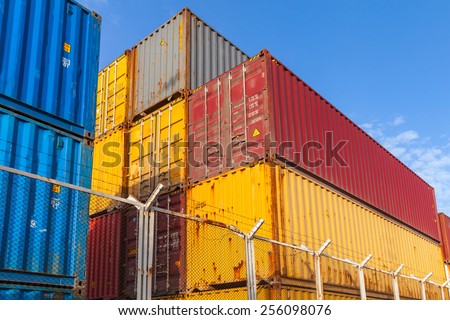 Colorful industrial cargo containers are stacked behind metal fence with barbed wire