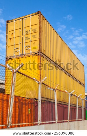 Metal industrial cargo containers are stacked under blue cloudy sky. Vertical photo