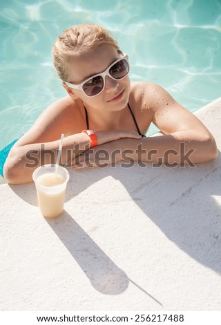 Little blond girl with glass of cocktail in swimming pool, vintage toned photo filter effect
