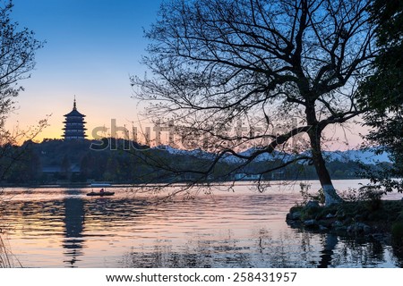 Black trees silhouette and traditional Chinese pagoda on the coast of West Lake. Famous park in Hangzhou city center, China