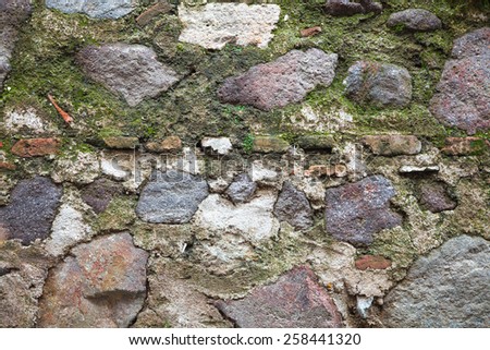 Old fortress wall made of dark gray stones with green moss, detailed background texture