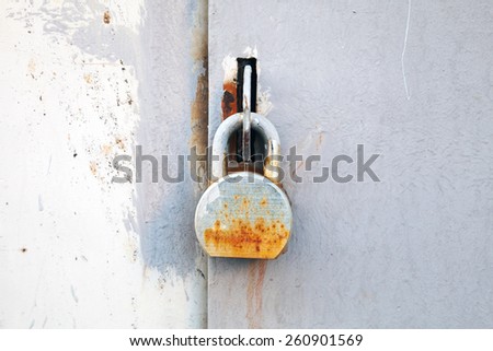 Old rusted padlock hanging on gray metal industrial door