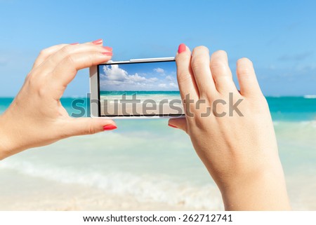Woman using cell phone for taking sea landscape photo on a beach in Dominican republic
