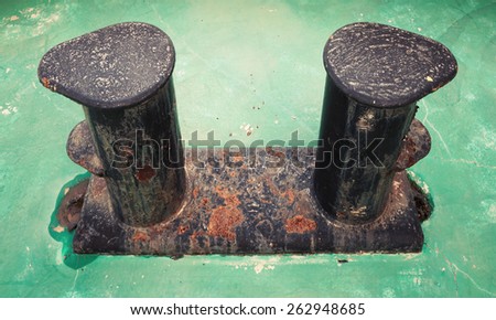 Old black rusted bollard mounted on green ship deck