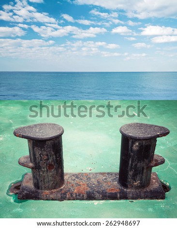 Old black rusted bollard mounted on green ship deck, with sea landscape on a background