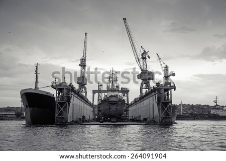Floating dry dock with old ship under repair inside, retro stylized black and white photo, front view