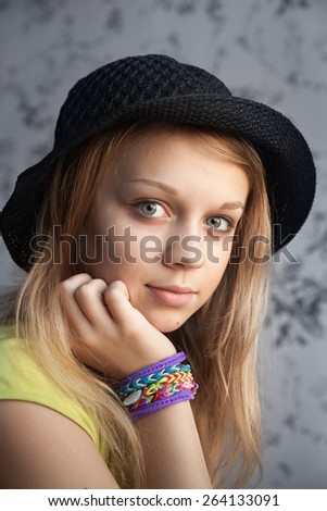 Portrait of beautiful blond teenage girl in black hat and rubber loom bracelets, vintage toned photo filter, instagram style effect