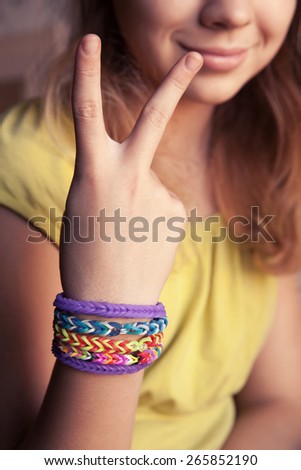 Caucasian girl showing two fingers with colorful rubber rainbow loom bracelets on her wrist, trendy teenagers fashion accessories. Vintage retro tonal photo filter correction, instagram style