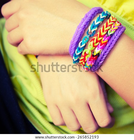 Child hands with Colorful rubber rainbow loom band bracelets, trendy kids fashion accessories.  Vintage retro tonal photo filter correction, instagram style