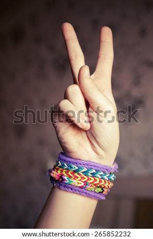 Child hand showing victory sign with colorful rubber rainbow loom bracelets on wrist, trendy teenagers fashion accessories. Vintage retro tonal photo filter correction, instagram style