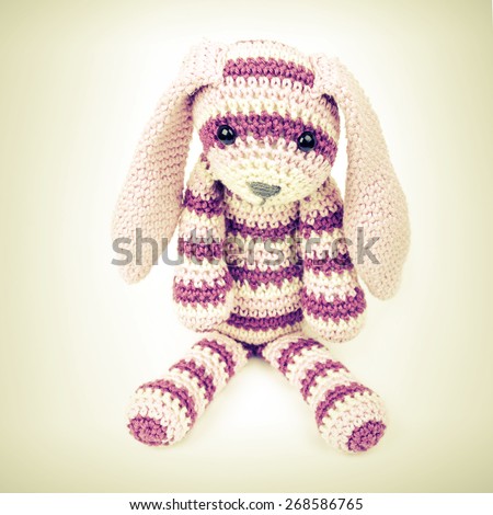 Knitted rabbit toy sitting over white background with soft shadow, vintage toned square photo with instagram retro style toned effect